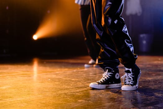 Danseurs en Krump sur scène, mettant en avant des chaussures de sport et des pantalons amples, éclairage dynamique en arrière